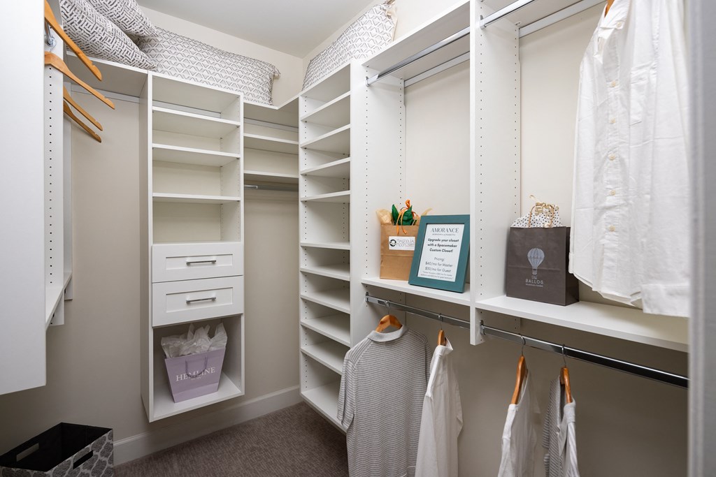 a walk in closet with white shelves and a window
