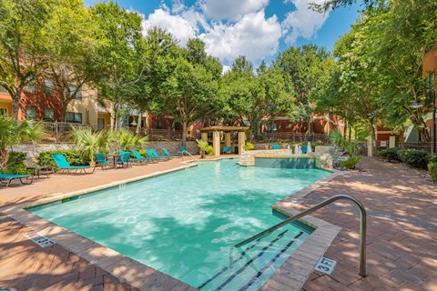 A swimming pool surrounded by trees and lounge chairs.