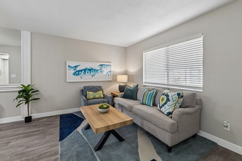 A living room with a grey couch, a wooden coffee table, and a painting of a fish on the wall.
