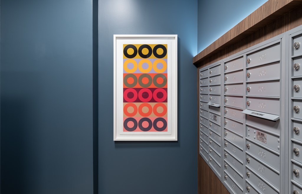 A framed picture of circles in different colors is hanging on a wall next to a row of mailboxes.