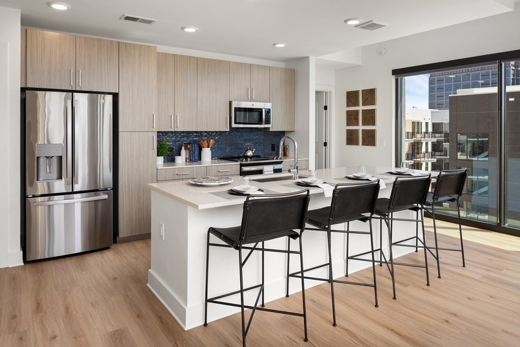 a kitchen with a large island with bar stools and a stainless steel refrigerator