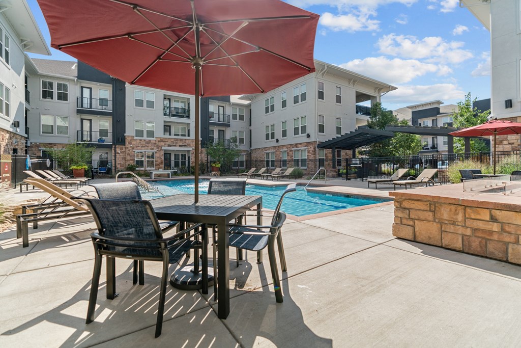 a patio with a table and chairs and a pool in the background