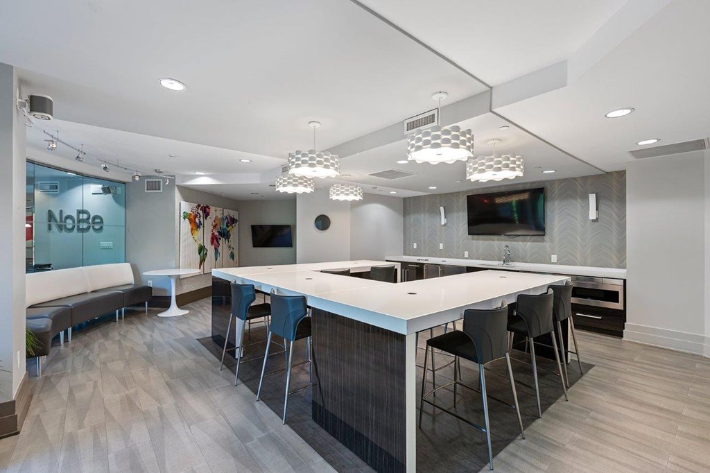 A modern kitchen with a long white island and black chairs.