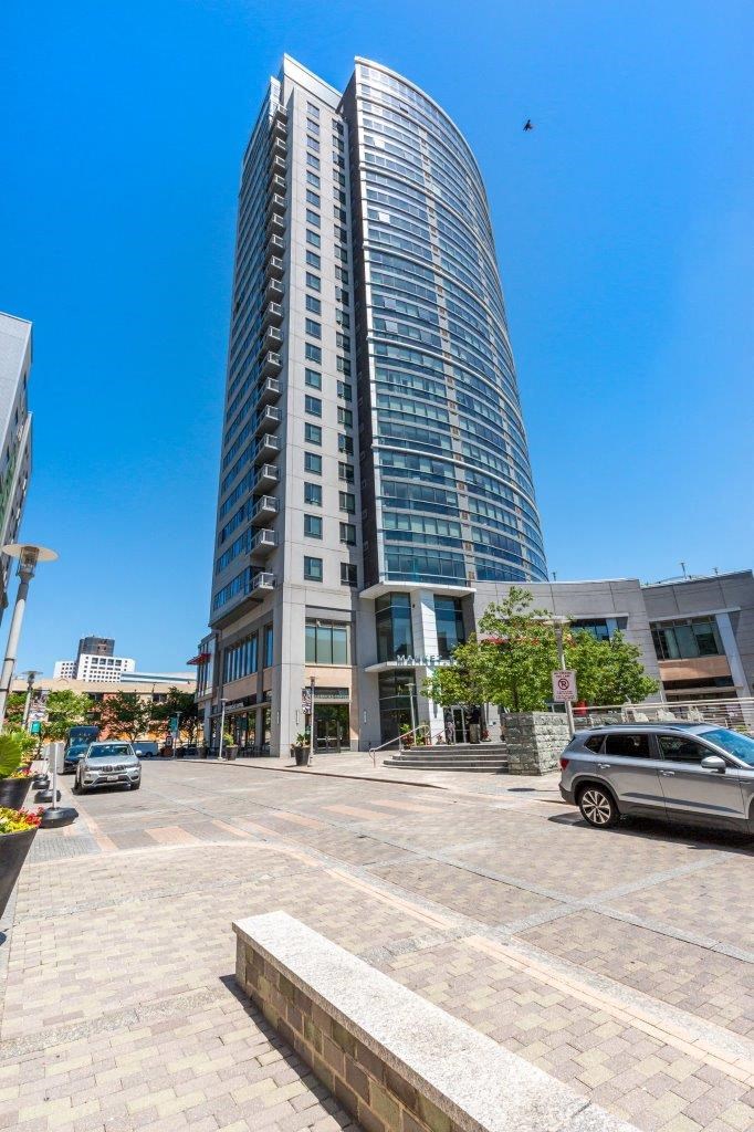 A tall, curved glass building stands in the middle of a city street.