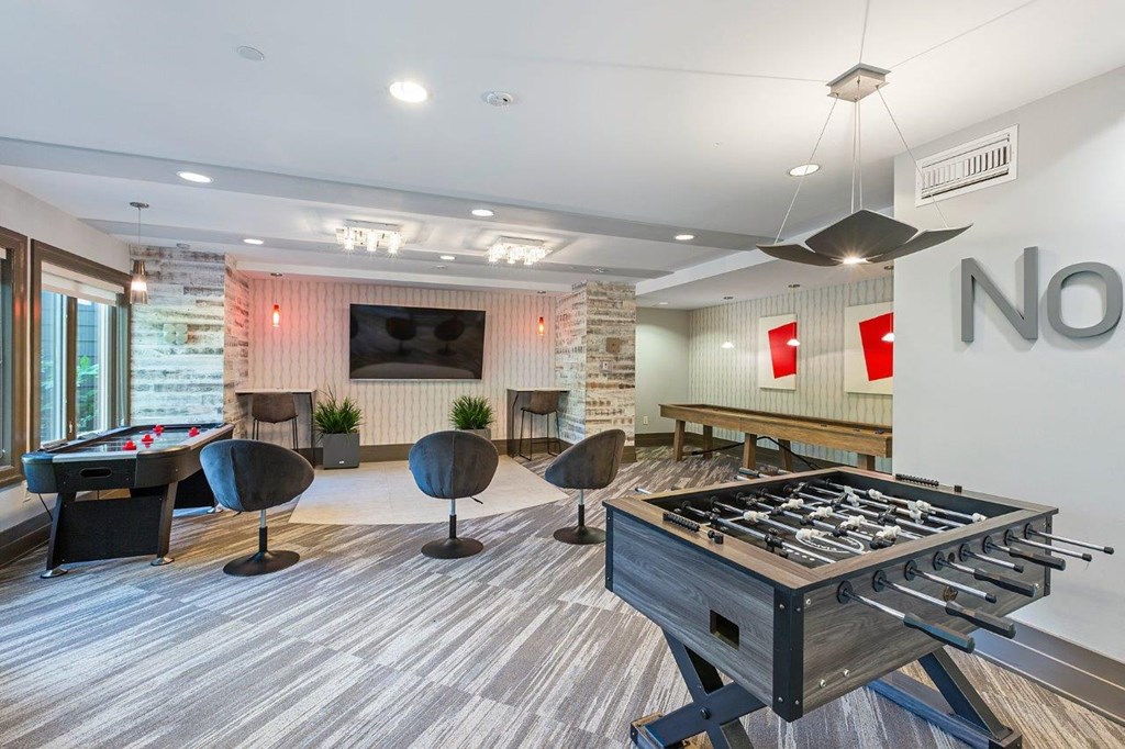 A foosball table is in the middle of a room with a pool table and a couch.