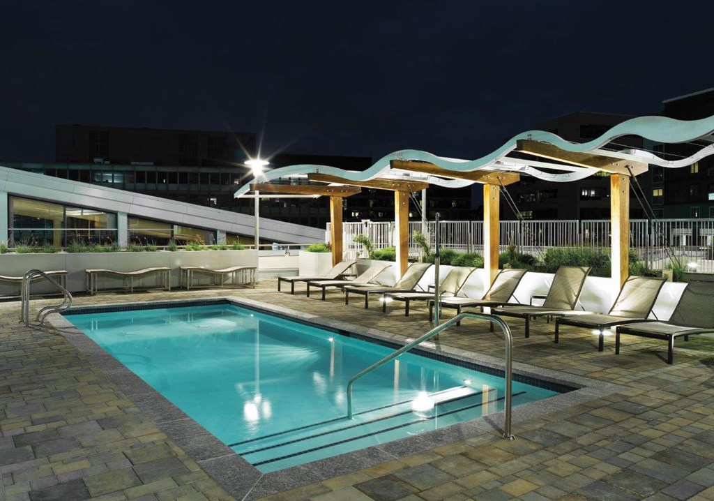 A pool with a wooden pergola and lounge chairs.