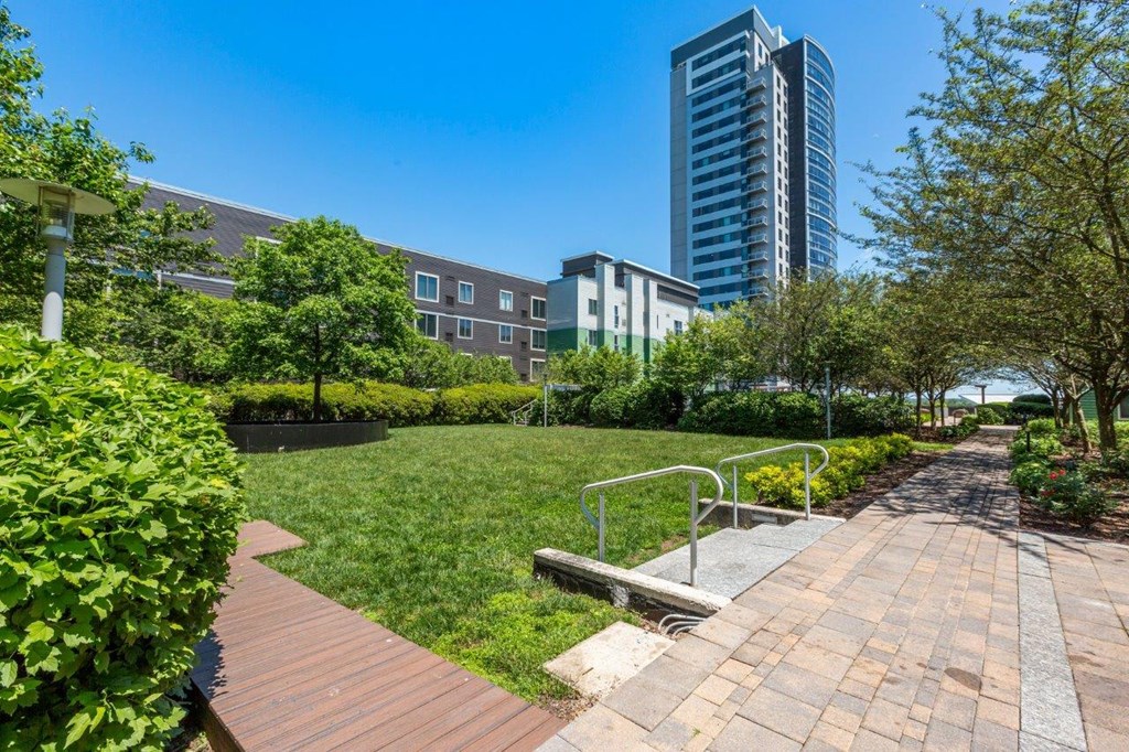 A park with a wooden walkway and a bench in the foreground with a cityscape in the background.