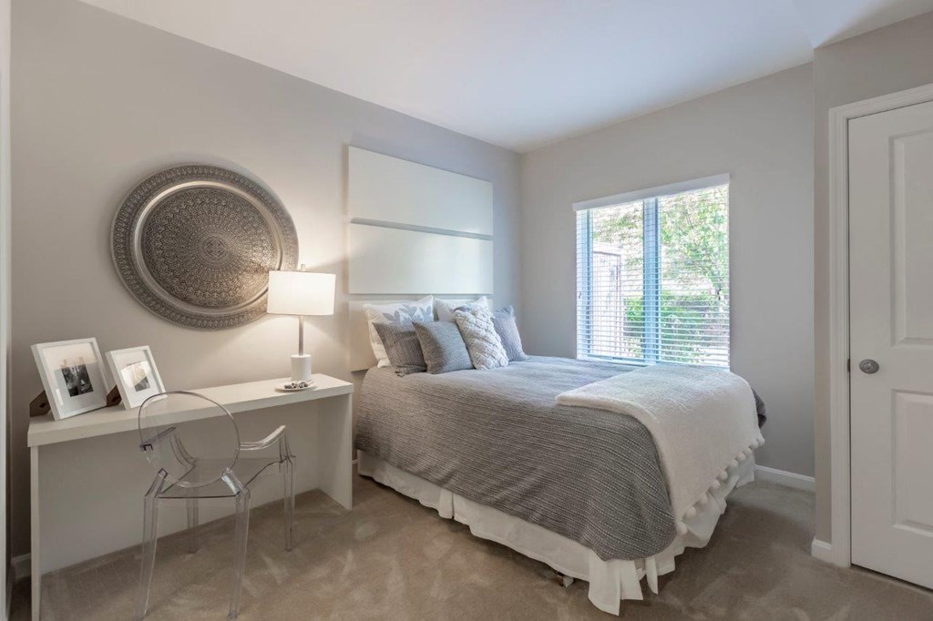 A bedroom with a bed, desk, chair, and window.