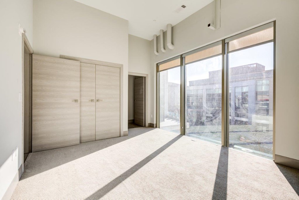 A room with a carpeted floor, a sliding glass door, and a wall-mounted air conditioning unit.