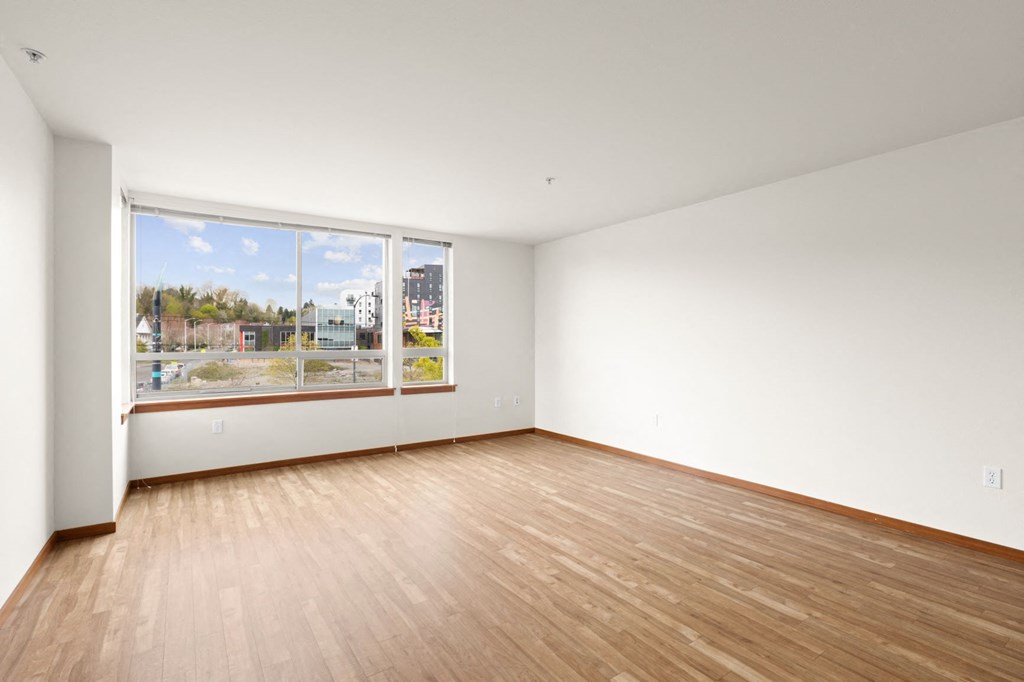 an empty bedroom with a large window and hardwood floors