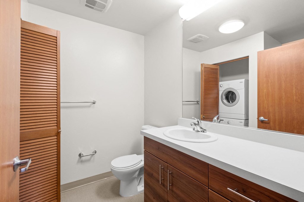 a bathroom with a toilet sink mirror and a washer and dryer