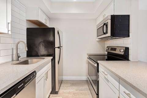 A black refrigerator stands next to a sink in a kitchen.
