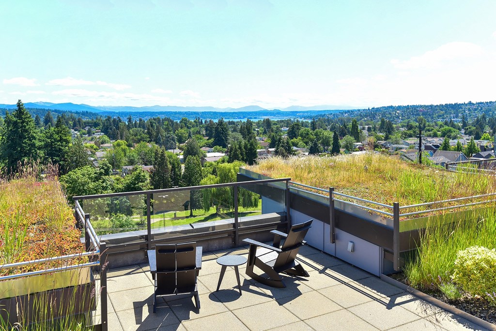 a rooftop deck with two chairs and a table with a view of the city