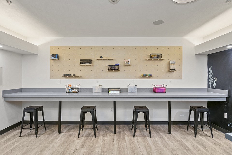 a long table with four stools in front of a wall with a pegboard on it