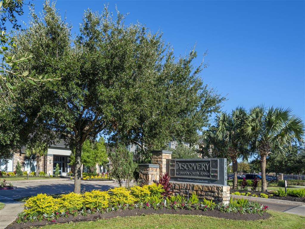 a sign in front of a park with trees and flowers