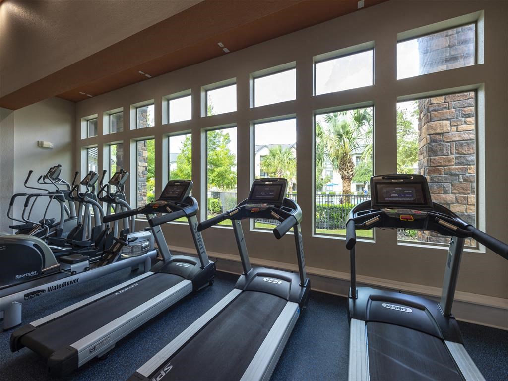 a gym with cardio equipment and large windows
