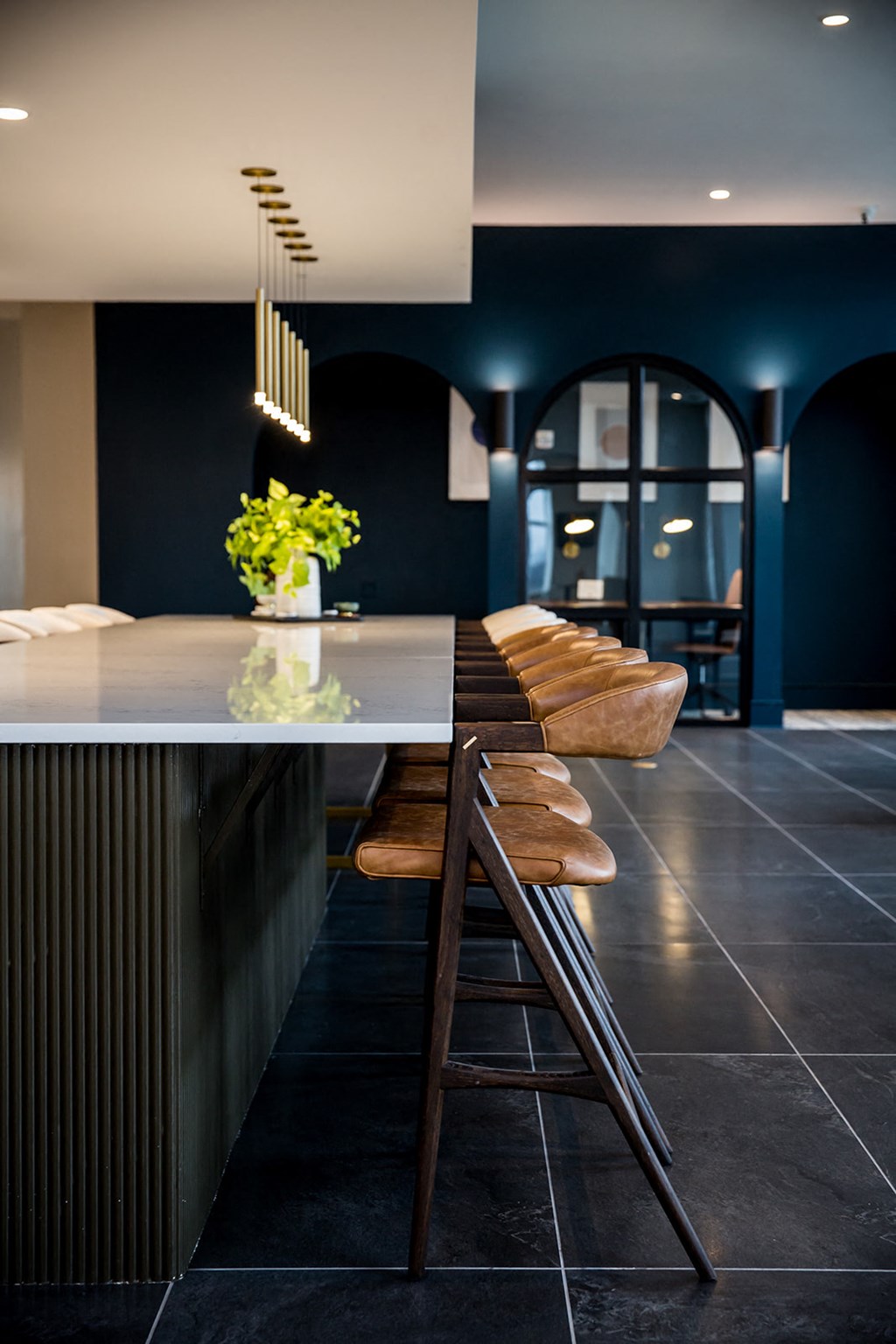 a dark blue kitchen with a white countertop and wooden stools