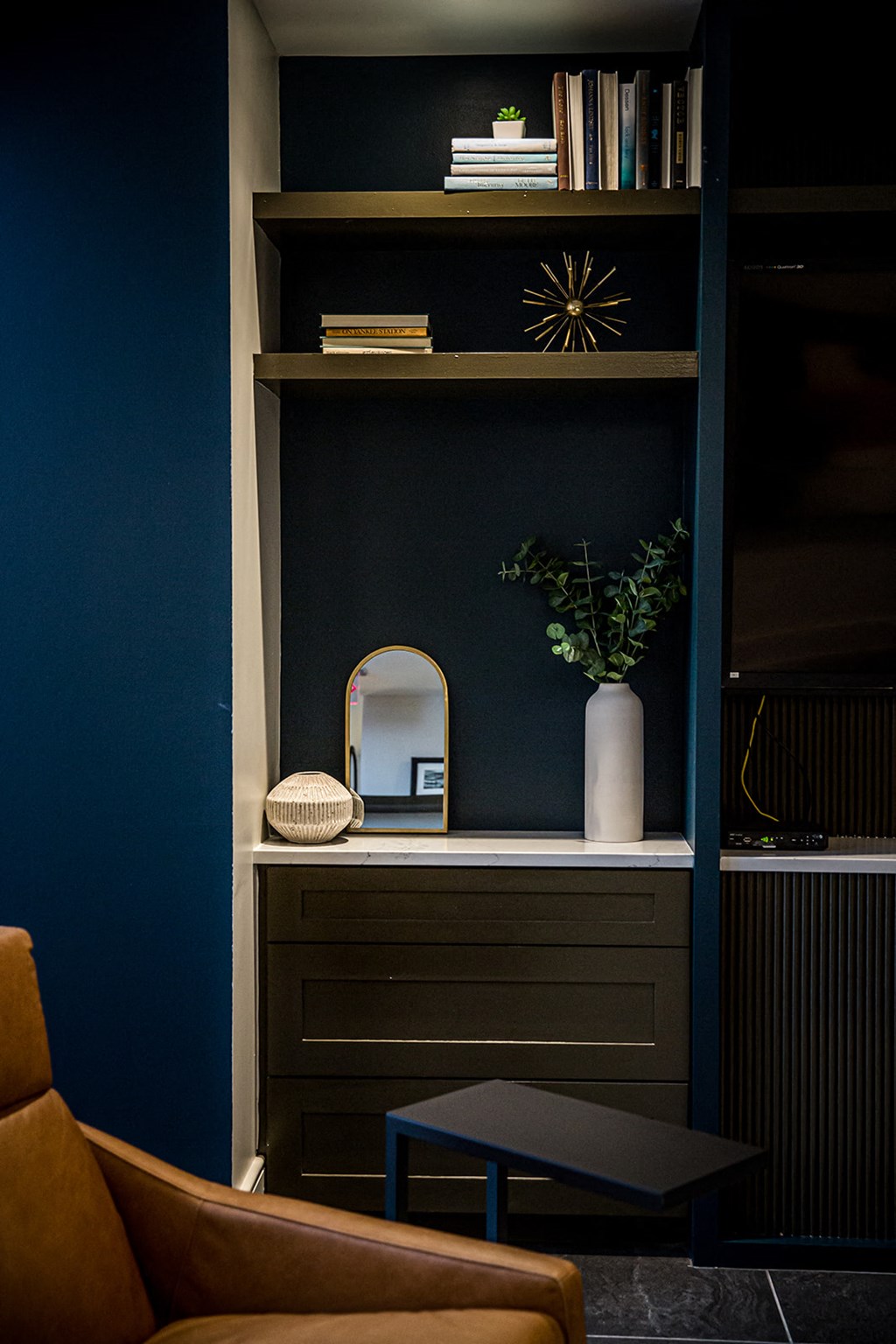 a dark blue bookshelf with a mirror and a vase of flowers