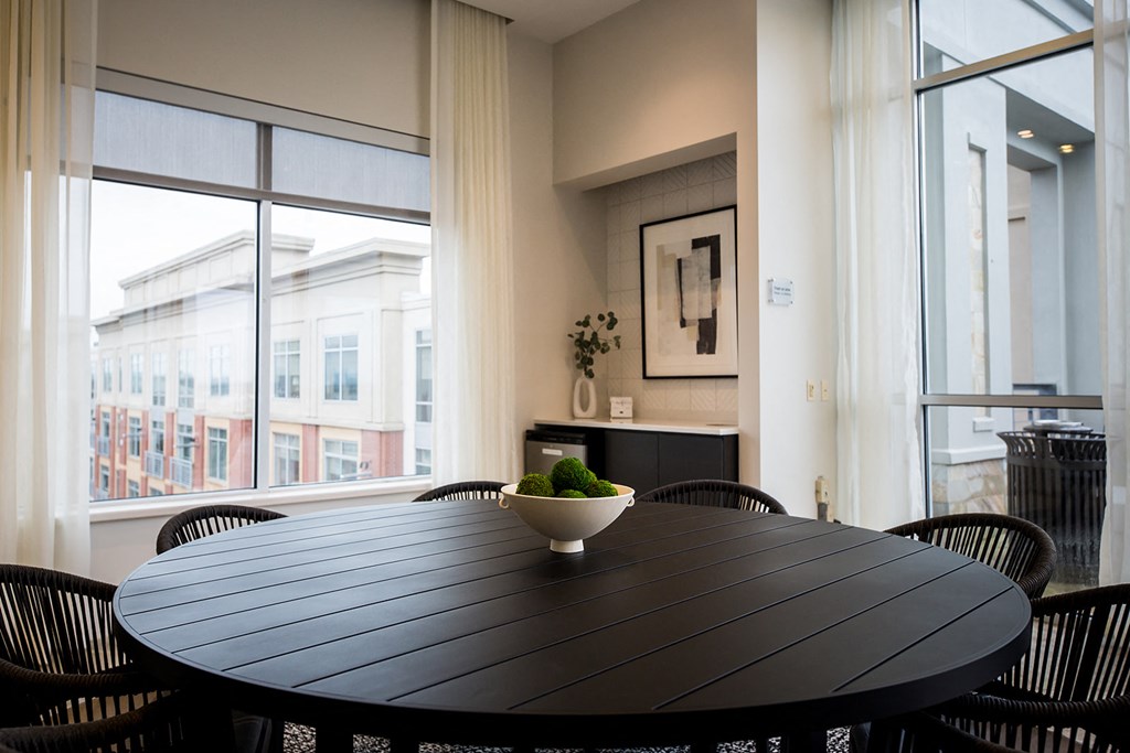 a table with a bowl of broccoli on it in a room with large windows