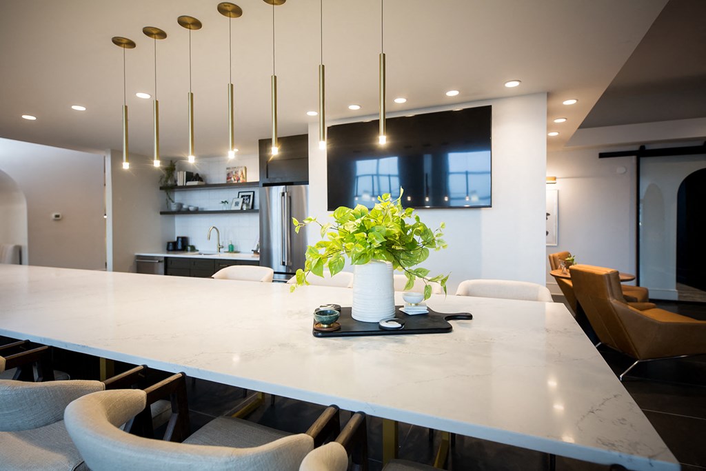 a long white table with chairs and a white vase with green flowers in the middle