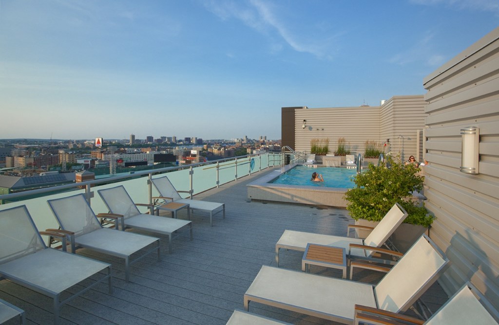 A rooftop patio with chairs and a pool overlooking a city skyline.