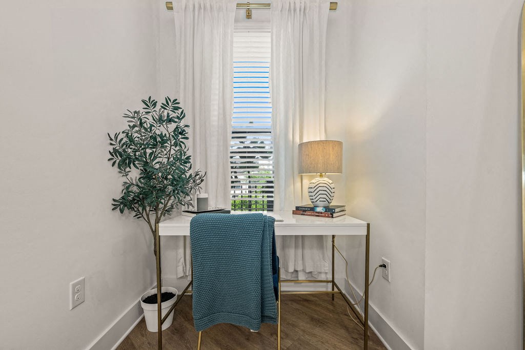A room with a table, a lamp, a plant and a chair.