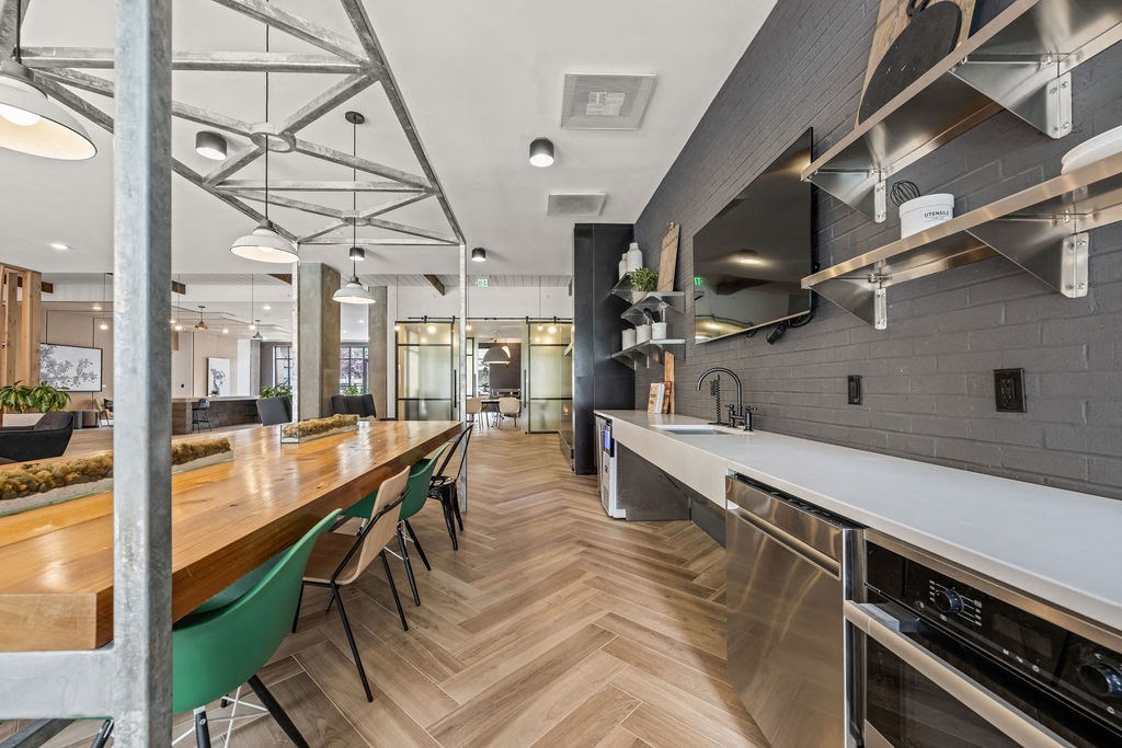 A long wooden table with green chairs is in a modern kitchen.