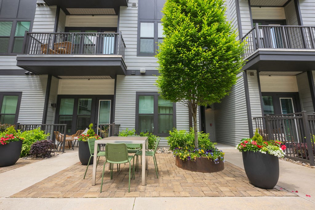 A patio with a table and chairs is surrounded by potted plants.