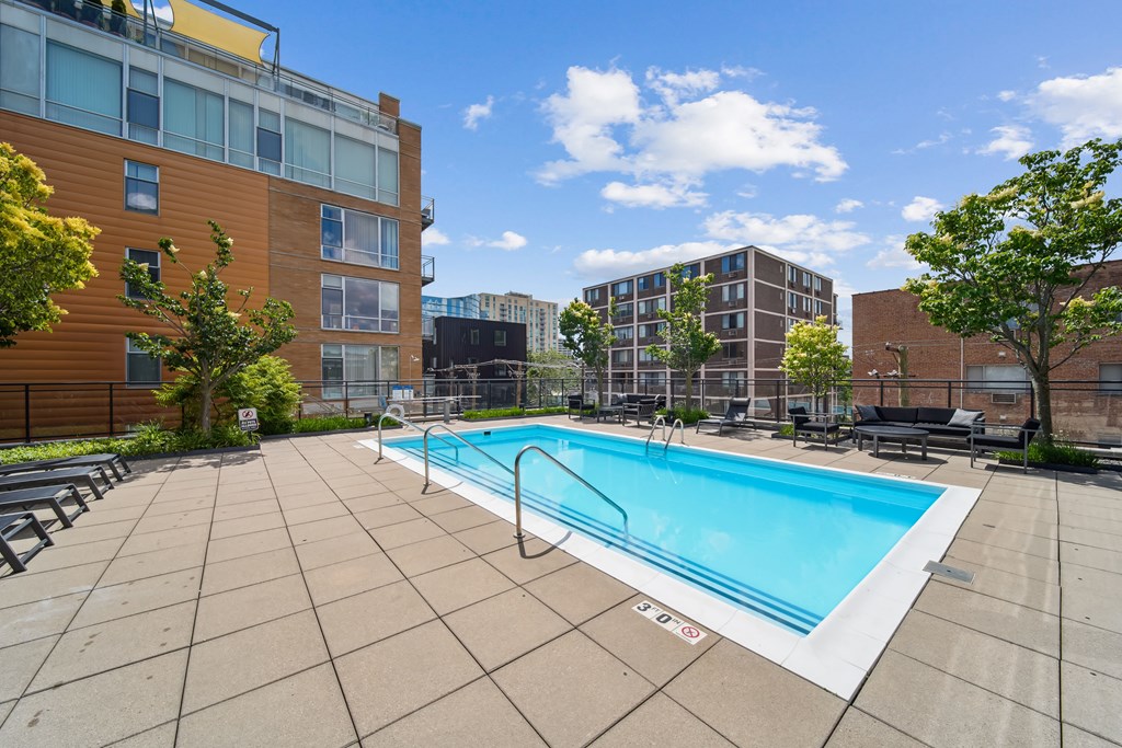 A swimming pool surrounded by a tiled patio and buildings in the background.