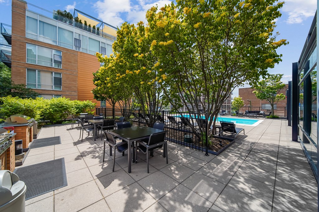 A patio with a table and chairs is surrounded by a pool and trees.