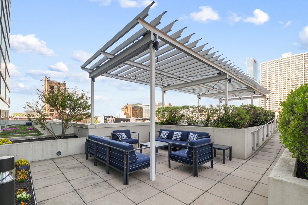 a pergola with blue lounge chairs and a coffee table on a patio with a city