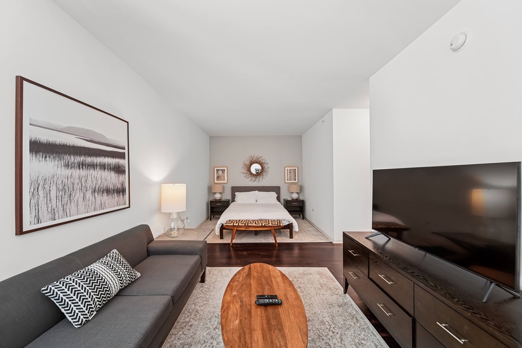 A modern living room with a grey couch, a wooden coffee table, and a large painting on the wall.