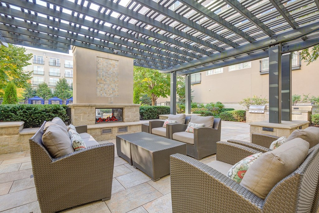 a patio with wicker furniture and a fireplace under a pergola