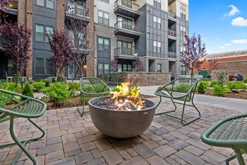 a fire pit and chairs on a brick patio with an apartment building in the background