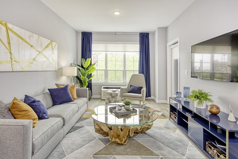 A modern living room with a grey couch, a glass coffee table, and a television.