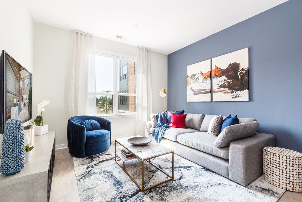 a living room with a blue accent wall and a gray couch at 100 House Apartments, Jersey City , NJ