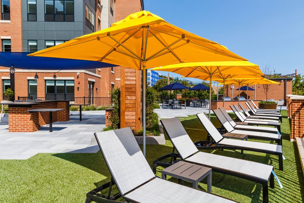 a row of lawn chairs with umbrellas in a courtyard at 100 House Apartments, New Jersey, 07310