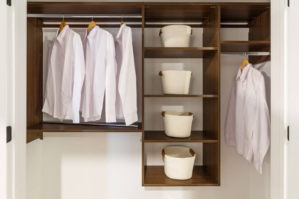 a closet with wooden shelves and baskets and white clothes