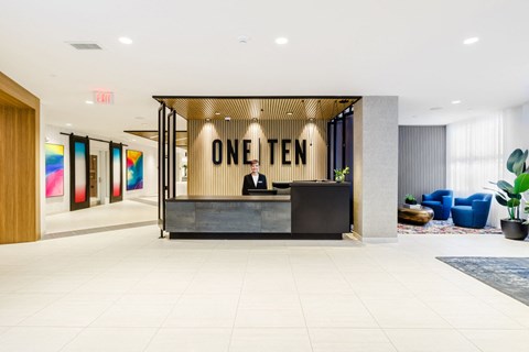 a man sitting at a desk in a lobby with a reception desk at One Ten Apartments, Jersey City , NJ, 07310