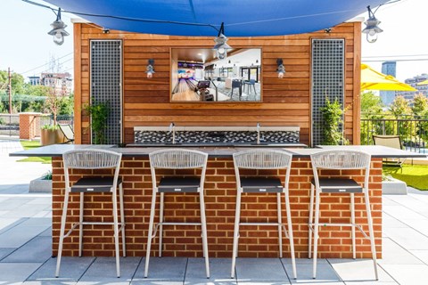 the outdoor bar is under a blue awning and a brick wall with chairs at One Ten Apartments, Jersey City , New Jersey