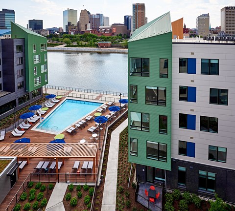 A green building with a pool in the foreground and a city skyline in the background.