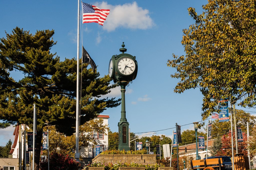 A large clock tower stands in front of a building with a flag flying in the background at The Reserve at Pearl River Apartments, Pearl River, NY