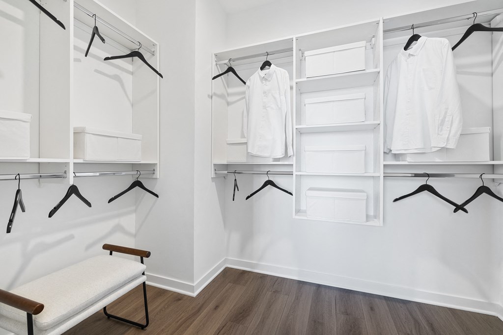 a white closet with white hangers and white shelves and a bench