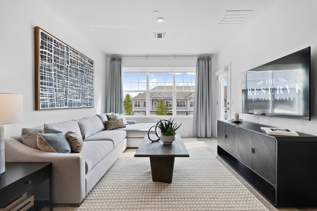 A modern living room with a large window overlooking a house at The Reserve at Pearl River Apartments, Pearl River, New York