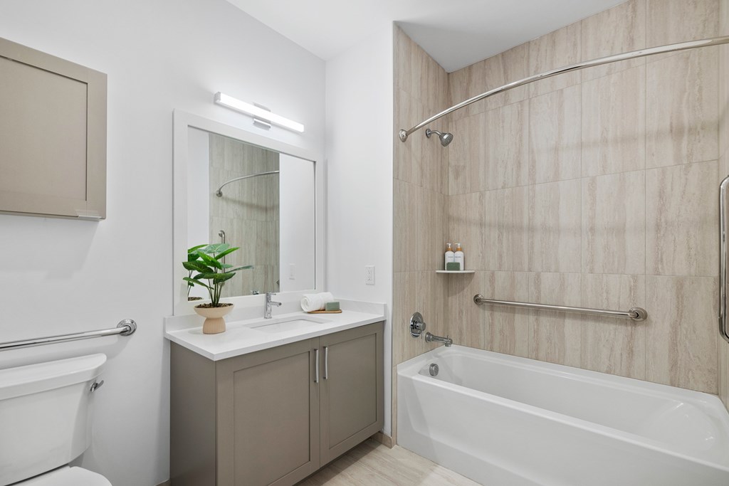 A bathroom with a white tub, sink, and a plant on the counter at The Reserve at Pearl River Apartments, New York, 10965
