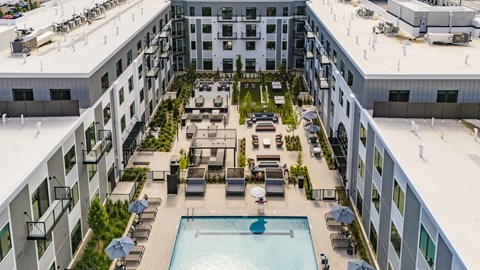 A large swimming pool is surrounded by lounge chairs and umbrellas in the middle of a courtyard.