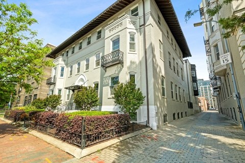 a grey apartment building with a brick sidewalk in front of it