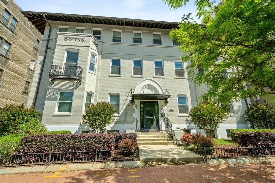 a gray building with a green door and a tree in front of it