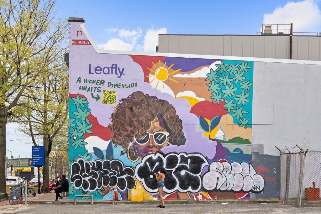 A mural of a person with a leafy hairstyle and the words "Leafly - A higher dimension awaits" on a wall.