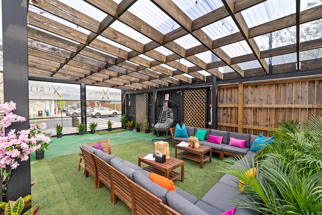 A wooden patio with a glass roof and a grey couch.